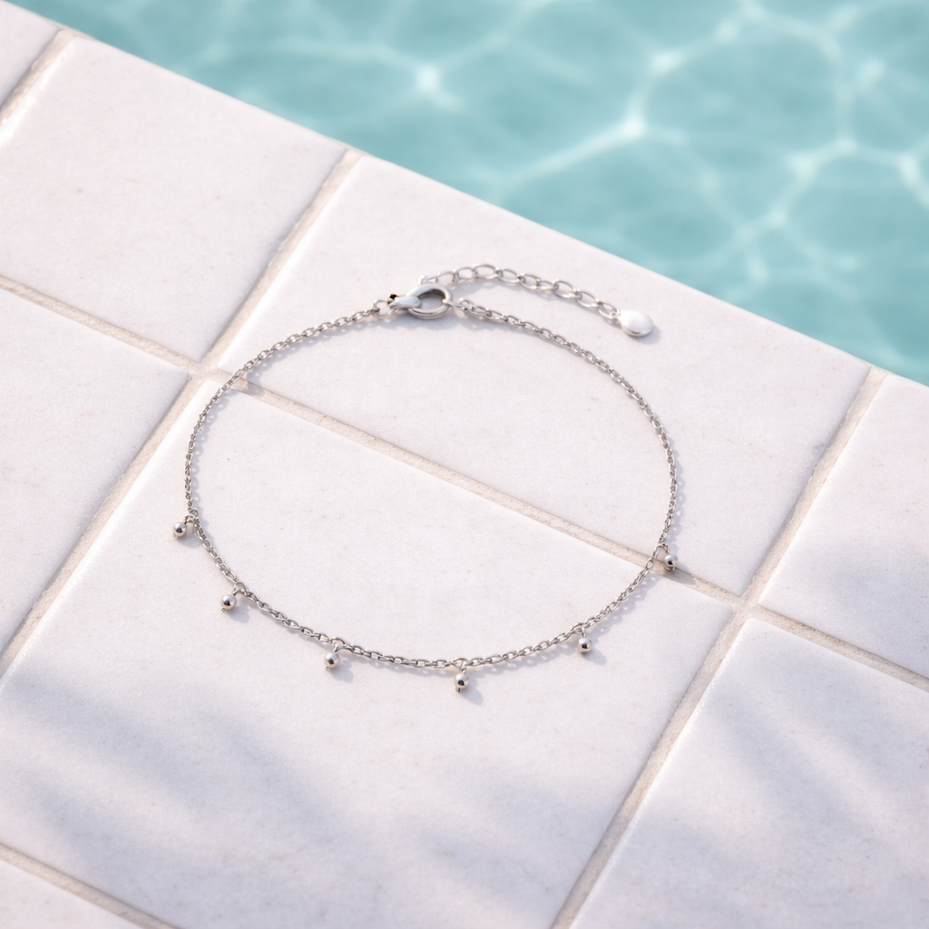 Chaîne de cheville argent 925 posée au bord d'une piscine sur un carrelage blanc, rappel de retirer ses bijoux avant de plonger