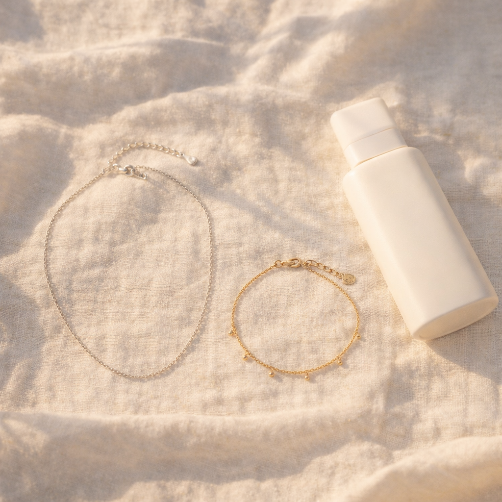 Tube de crème solaire posé à côté d'un bracelet plaqué or sur une serviette de plage, illustration des risques pour les bijoux