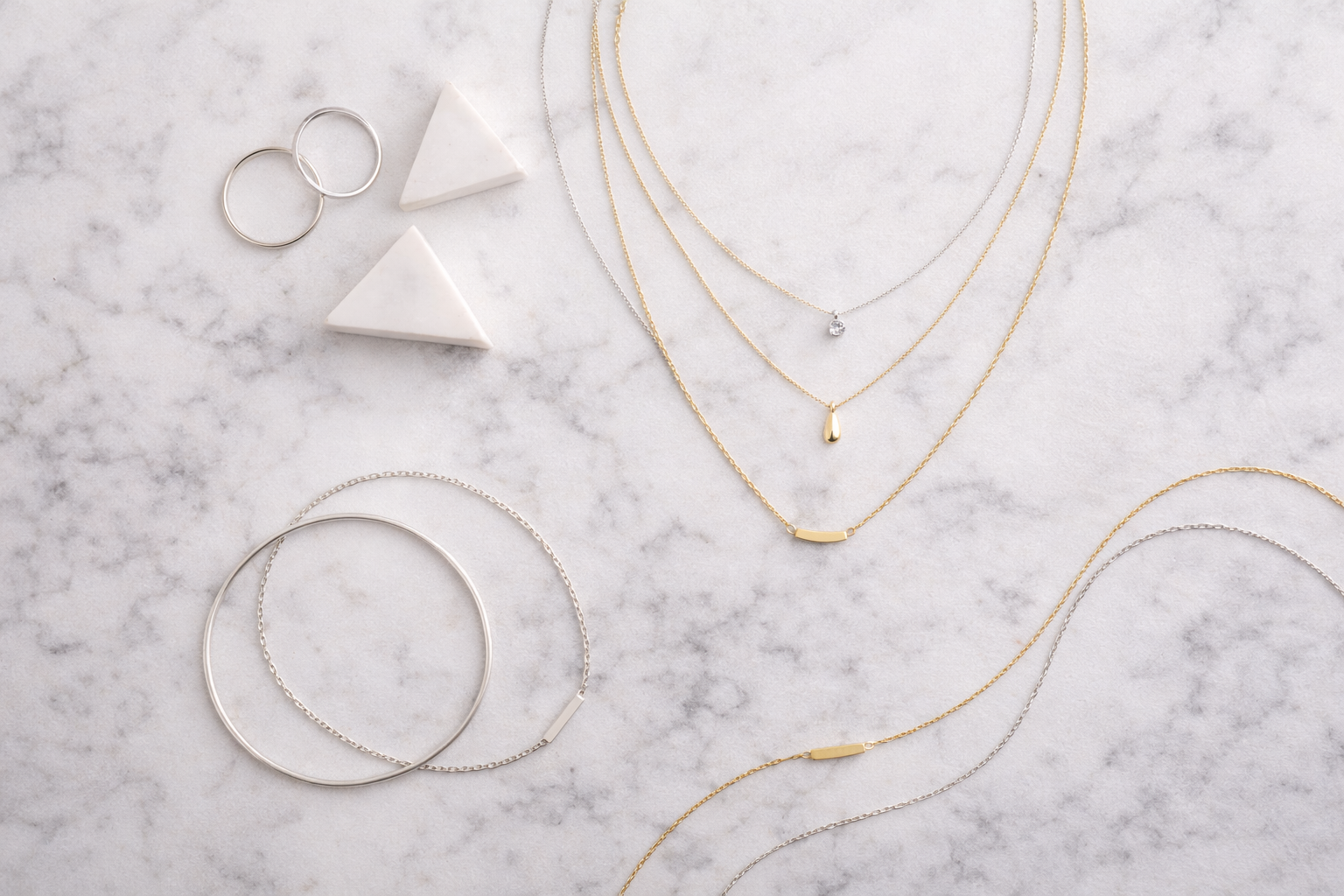 Composition flat lay de bijoux minimalistes en argent et or sur marbre blanc